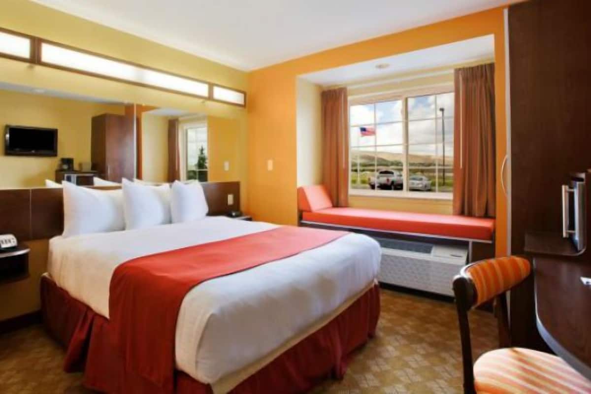 Habitación de hotel con una cama grande, un escritorio, una silla, un televisor y una ventana con vista a coches y colinas.