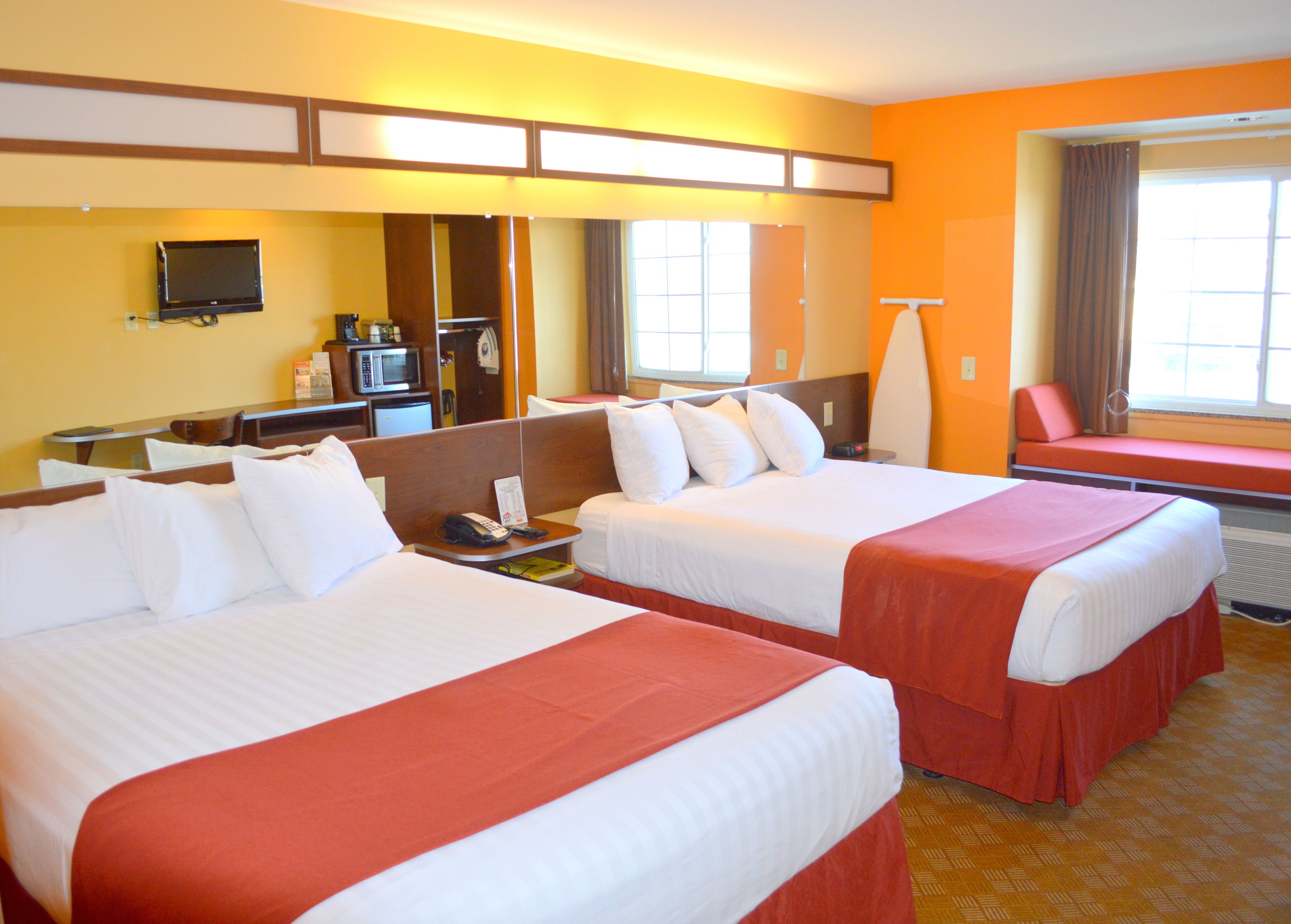 A hotel room with two beds, a desk, a microwave, a refrigerator, and a TV on the wall.