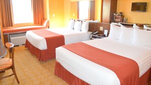 A hotel room with two beds, a desk, a chair, a television, and a window with curtains.