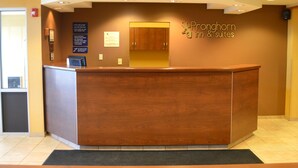 A reception desk with a wooden finish, a sign for 'Promhorm Inn & Suites', and a framed welcome message.