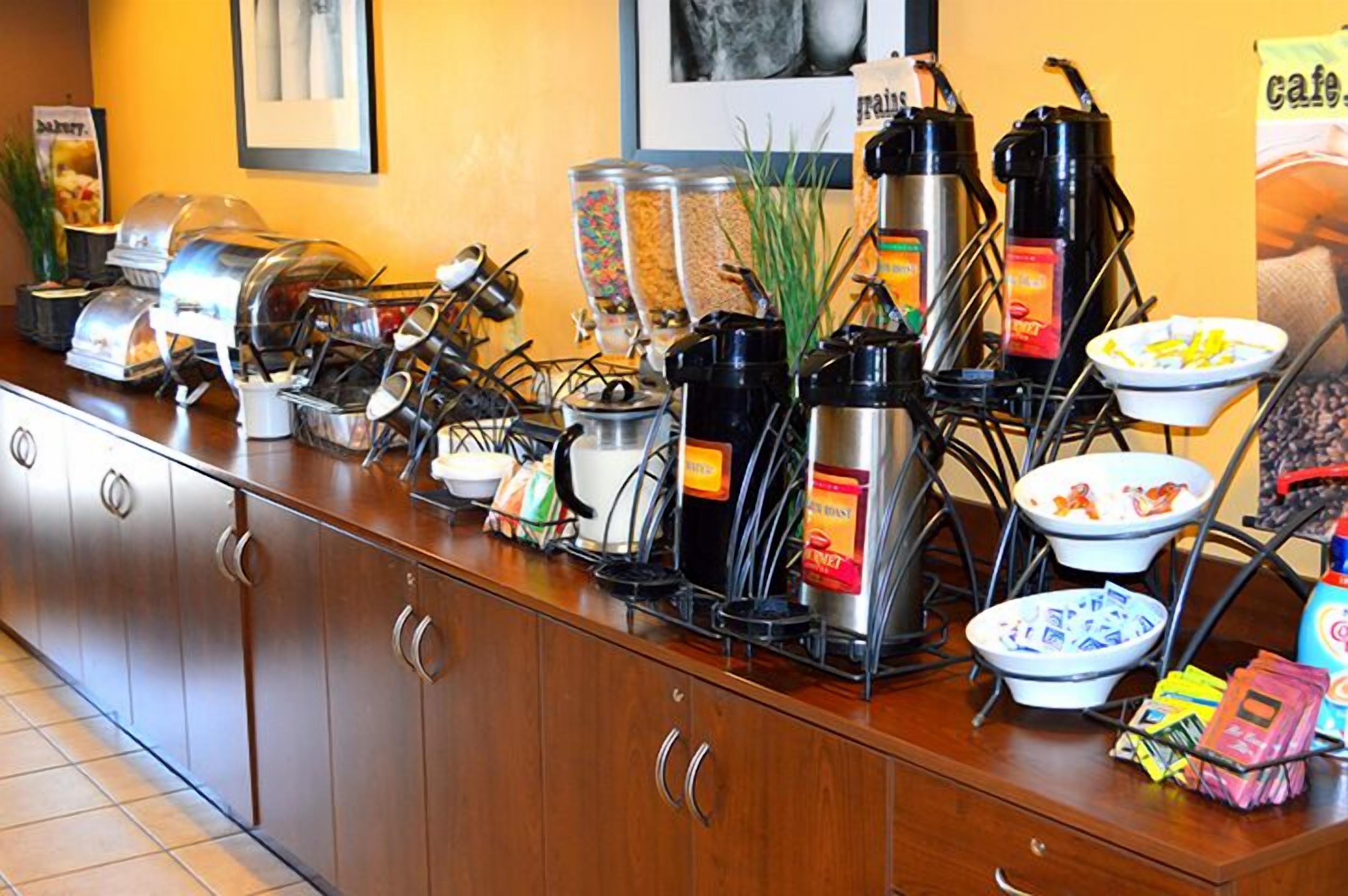 A buffet setup with various food containers, coffee machines, and condiments.