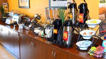A buffet setup with various food containers, coffee machines, and condiments.
