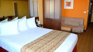 A hotel room with a large bed, a small desk, a chair, and a sofa.