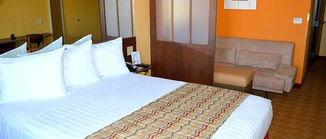 Habitación de hotel con una cama grande, un escritorio pequeño, una silla y un sofá.