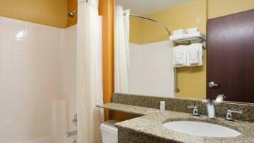 Casa de banho com banheira branca, lavatório com bancada de granito, espelho e toalheiro com toalhas dobradas.