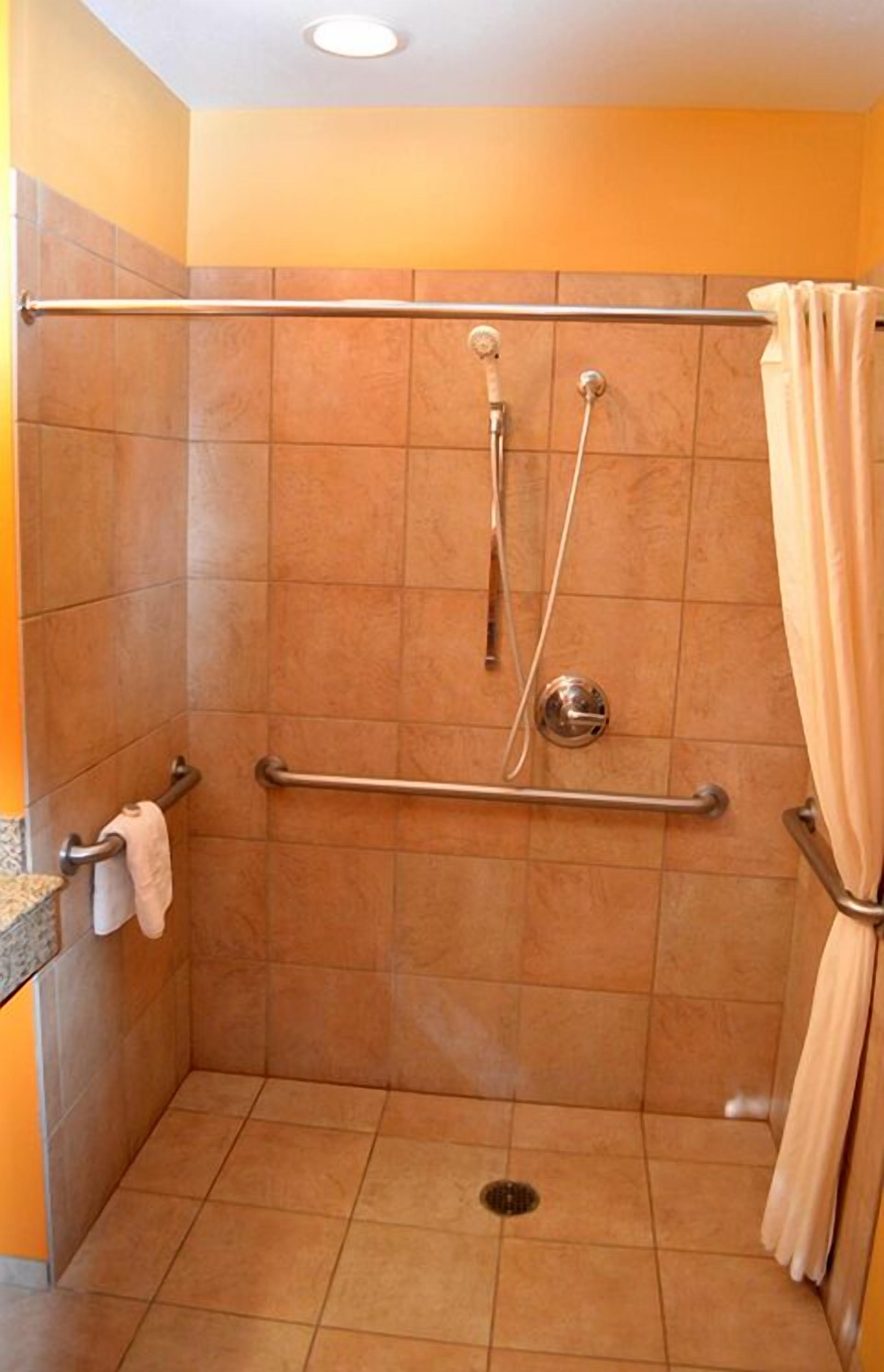 A shower with a grab bar, a towel rack, and a curtain.