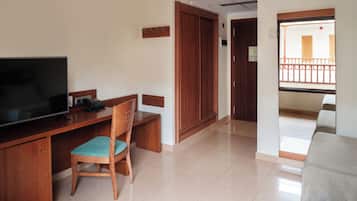 Quarto de hotel com uma escrivaninha de madeira, televisão, cadeira, sofá e varanda com guarda-corpo.