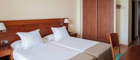 A double bed with white linens, a wooden headboard, a bedside table with a lamp, and a wooden wardrobe.