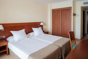 Una cama doble con sábanas blancas, un cabecero de madera, una mesita de noche con lámpara y un armario de madera.