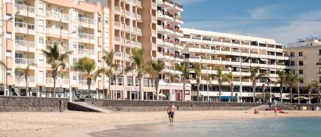A beachfront hotel with multiple balconies, a sandy beach, and palm trees.