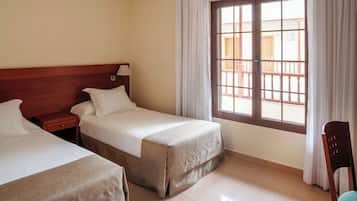 Een hotelkamer met twee enkele bedden, een houten hoofdbord, een nachtkastje, een raam met gordijnen en een stoel.