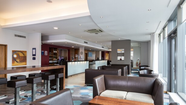 Un hall d’hôtel moderne avec des sièges en cuir, un bar et de grandes fenêtres.