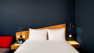 Una habitación de hotel con una cama, mesitas de noche, un teléfono y una silla roja.