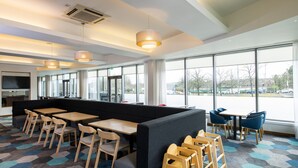 Un espace repas moderne avec des tables hautes, des chaises et un séparateur noir. De grandes fenêtres offrent une vue sur l’extérieur.