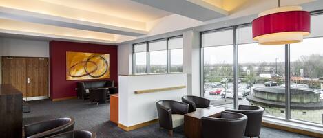 A modern hotel lobby with a reception desk, seating area, large windows, and a city view.