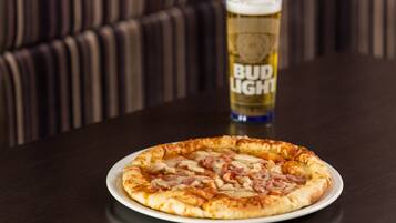 Une pizza sur une assiette blanche, avec un verre de bière Bud Light en arrière-plan.