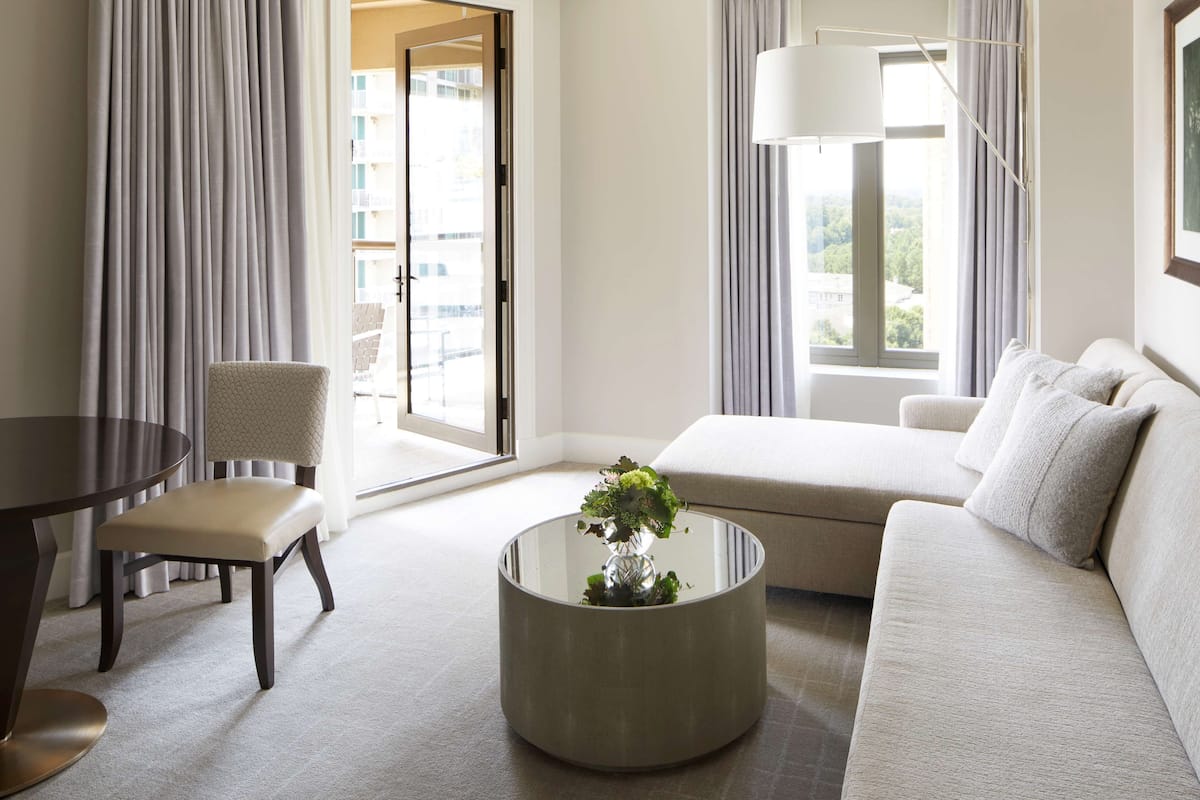 A modern living room with a round glass coffee table, a beige sofa, a round dining table, and a chair.