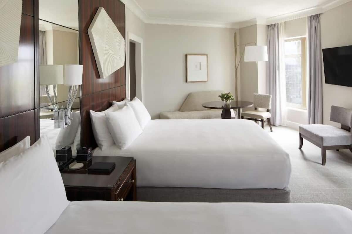 A hotel room with a large bed, a desk, a chair, a small table, a TV, and a window with curtains.