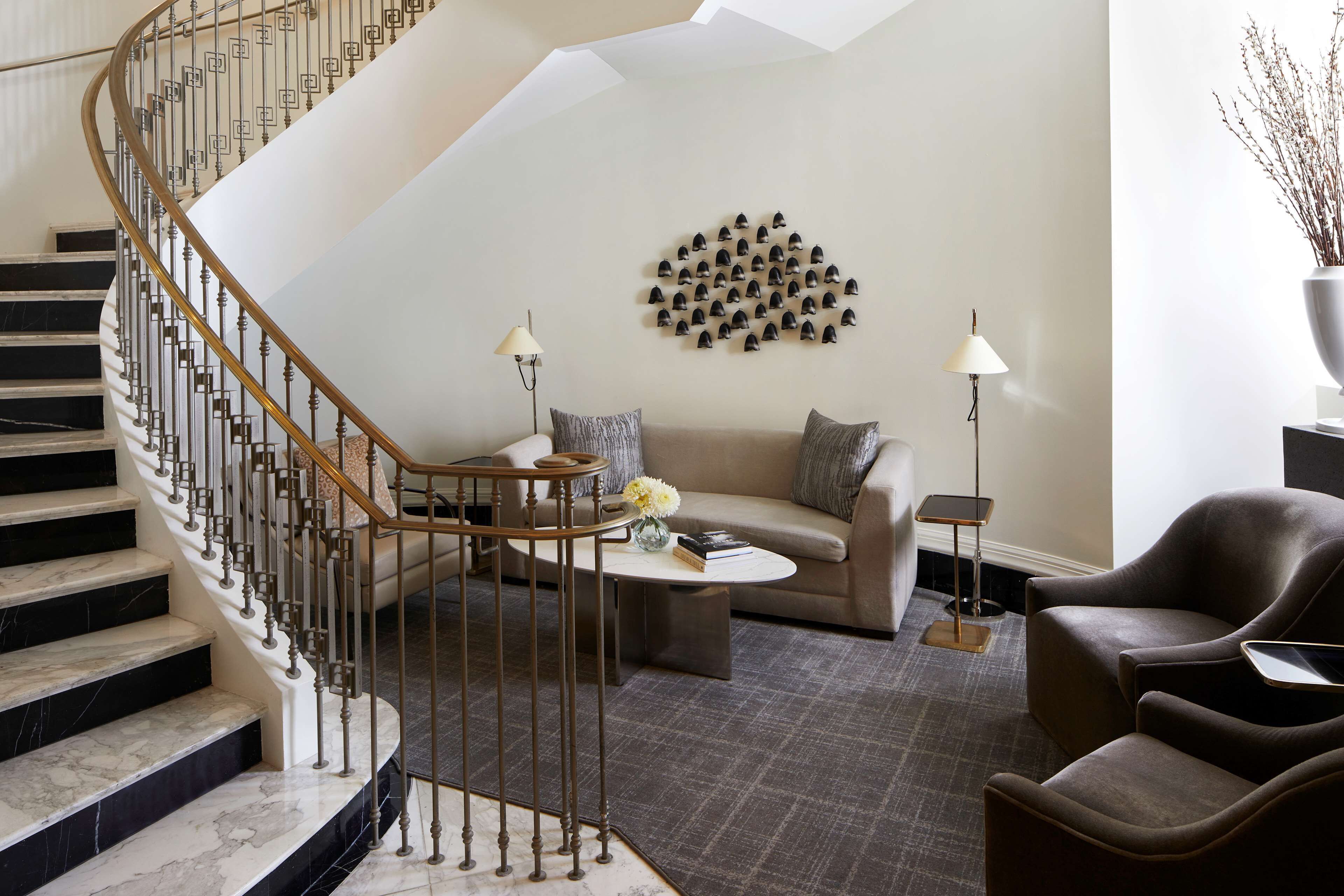 Una sala de estar moderna con una escalera de mármol, una mesa redonda para café, un sofá y un elemento decorativo en la pared.