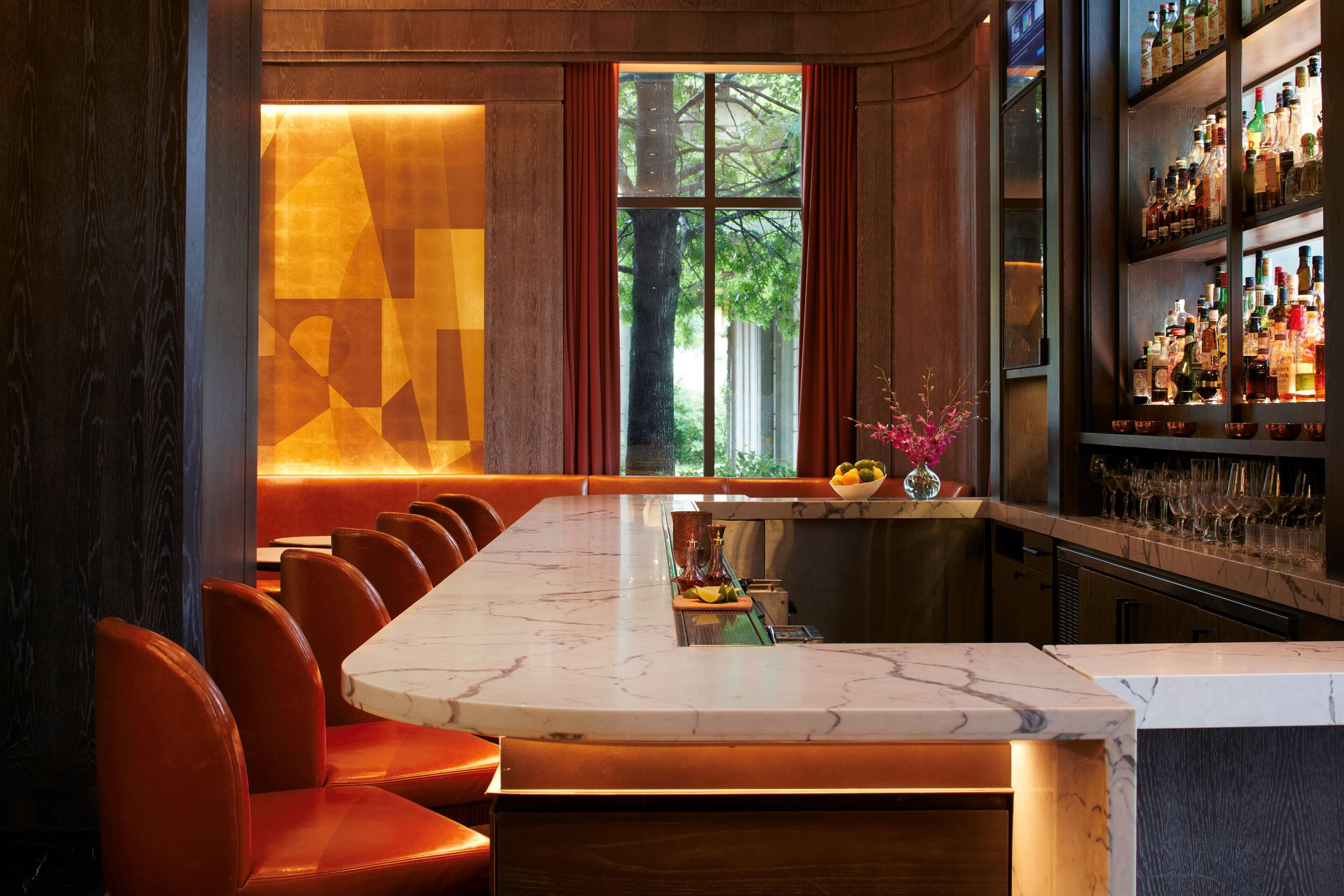 A bar with a marble countertop, leather chairs, and a view of trees through the window.