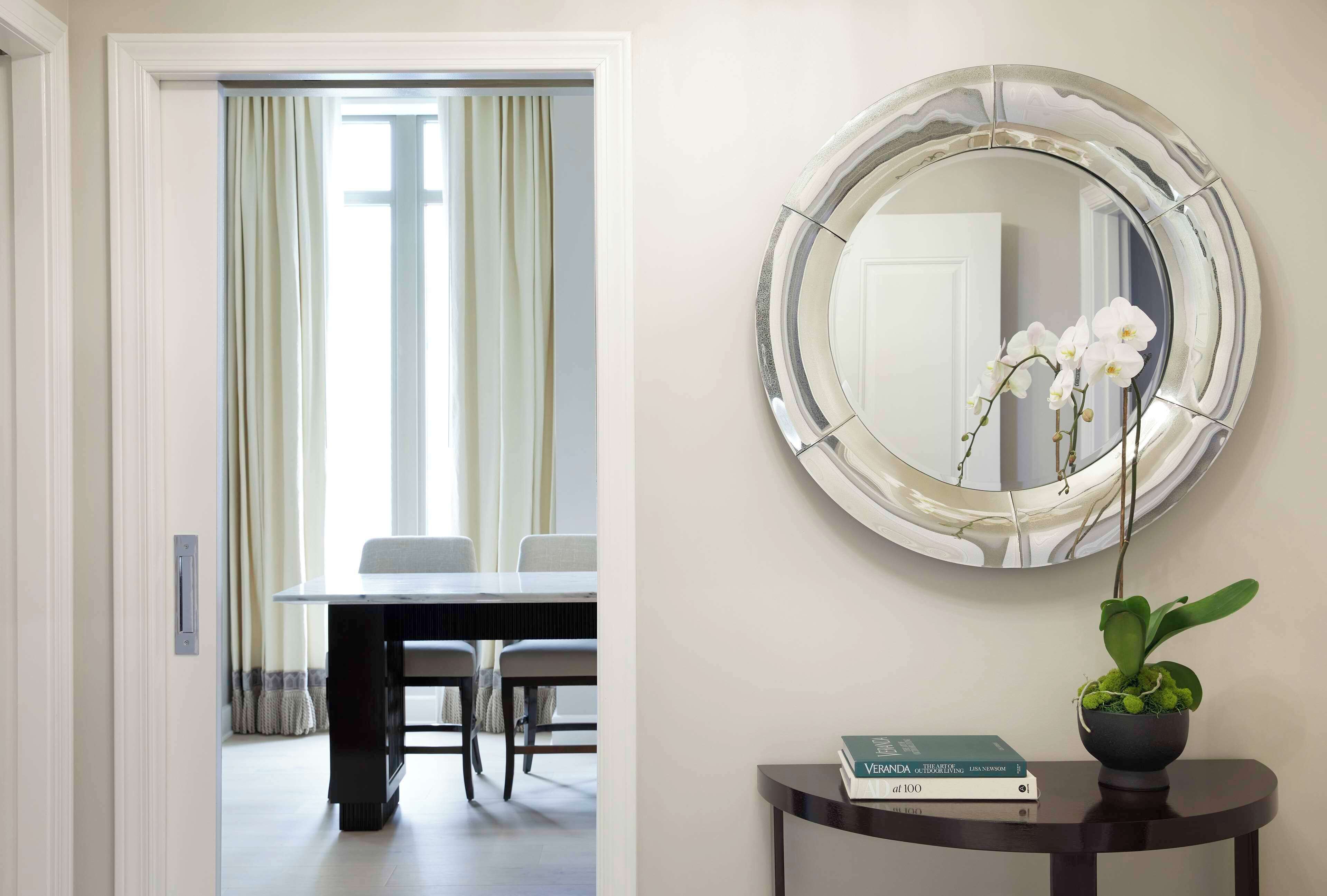 A hallway with a dining area, a round mirror, and a small table with a plant and books.