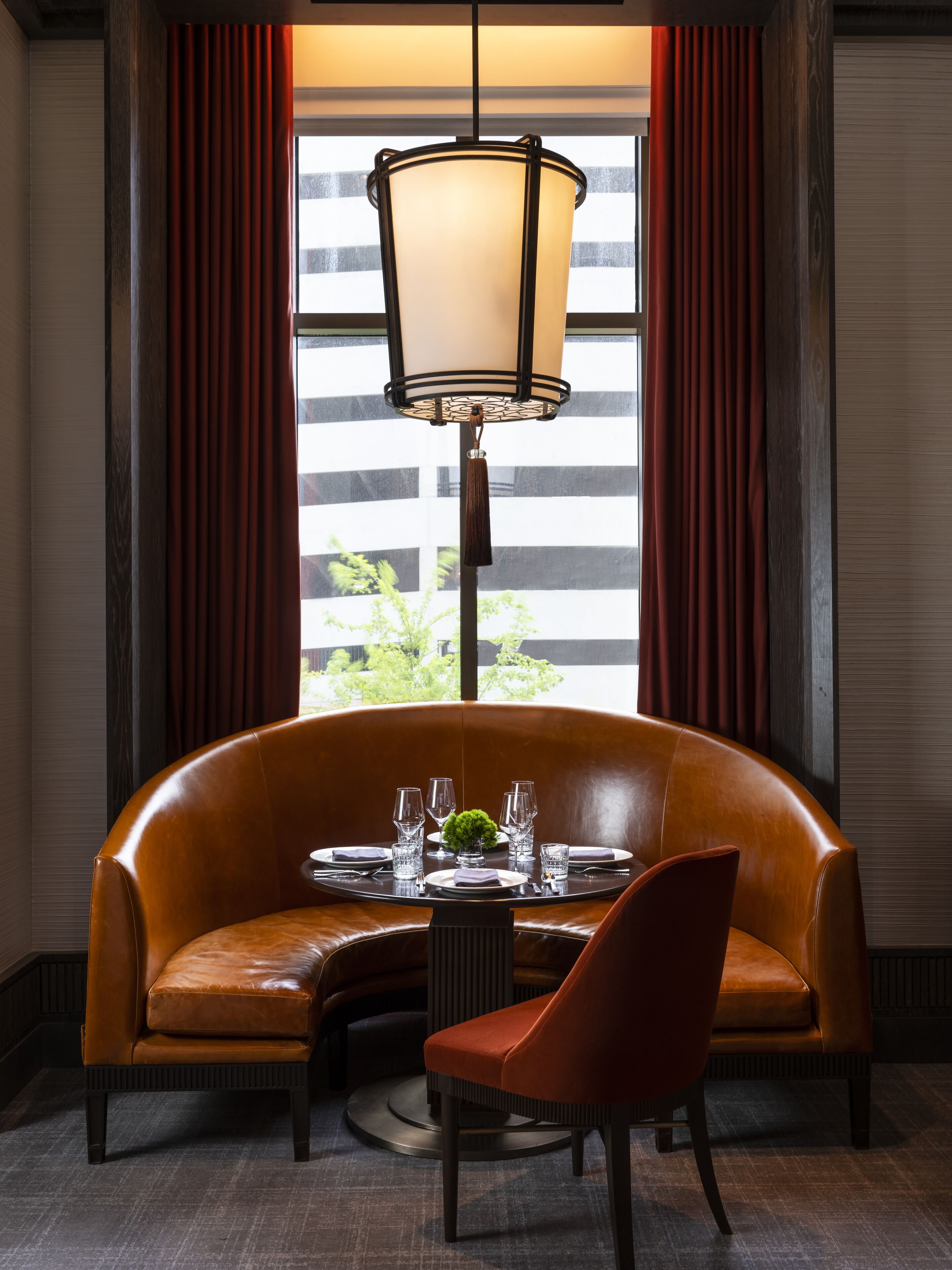 Un área de comedor con un sofá de cuero y una mesa preparada para dos, una lámpara colgante y una ventana con cortinas.