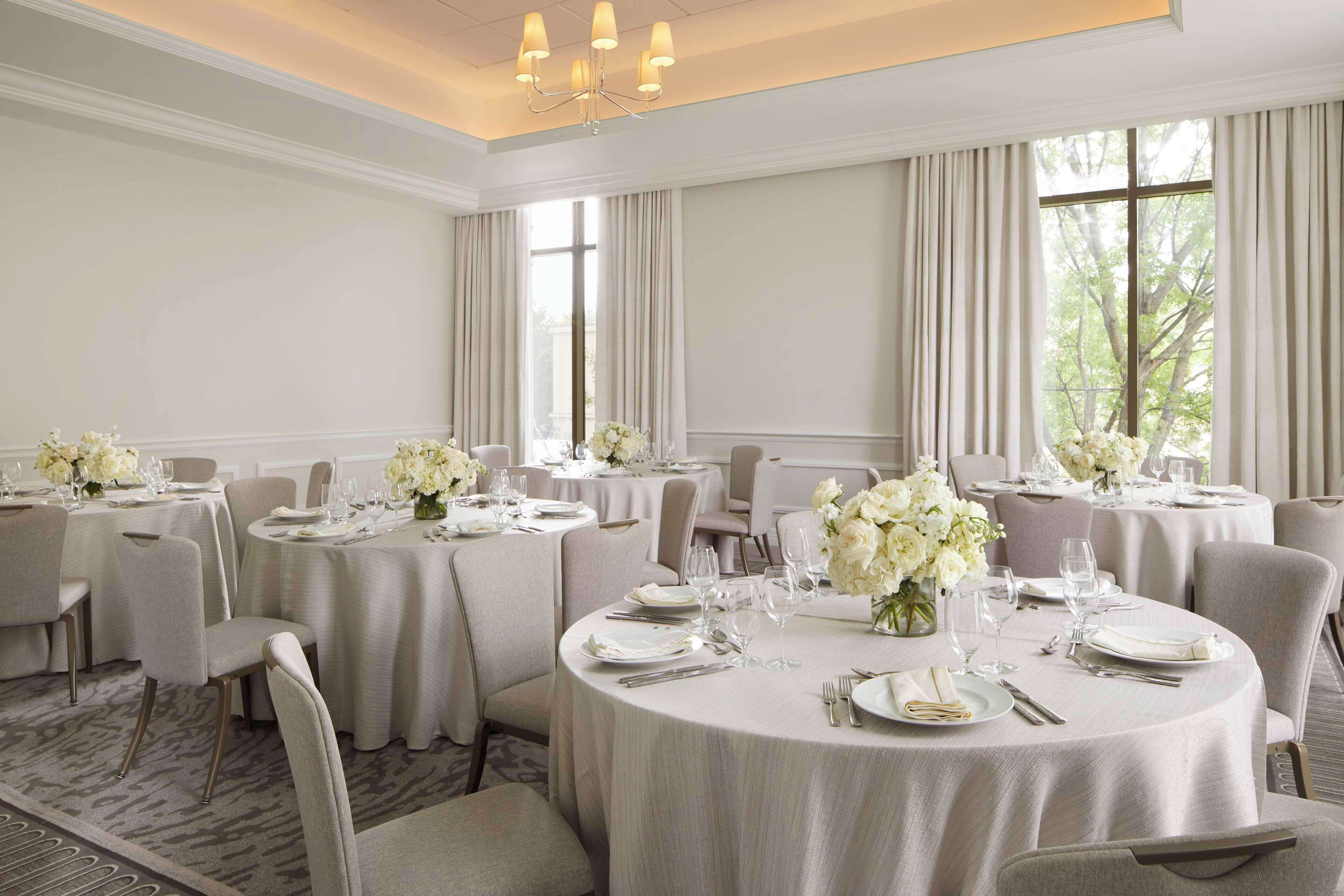 Ein Essbereich eines Hotels mit runden Tischen für vier Personen, jeweils mit weißen Tischdecken, Stühlen und floralen Tischdekorationen.