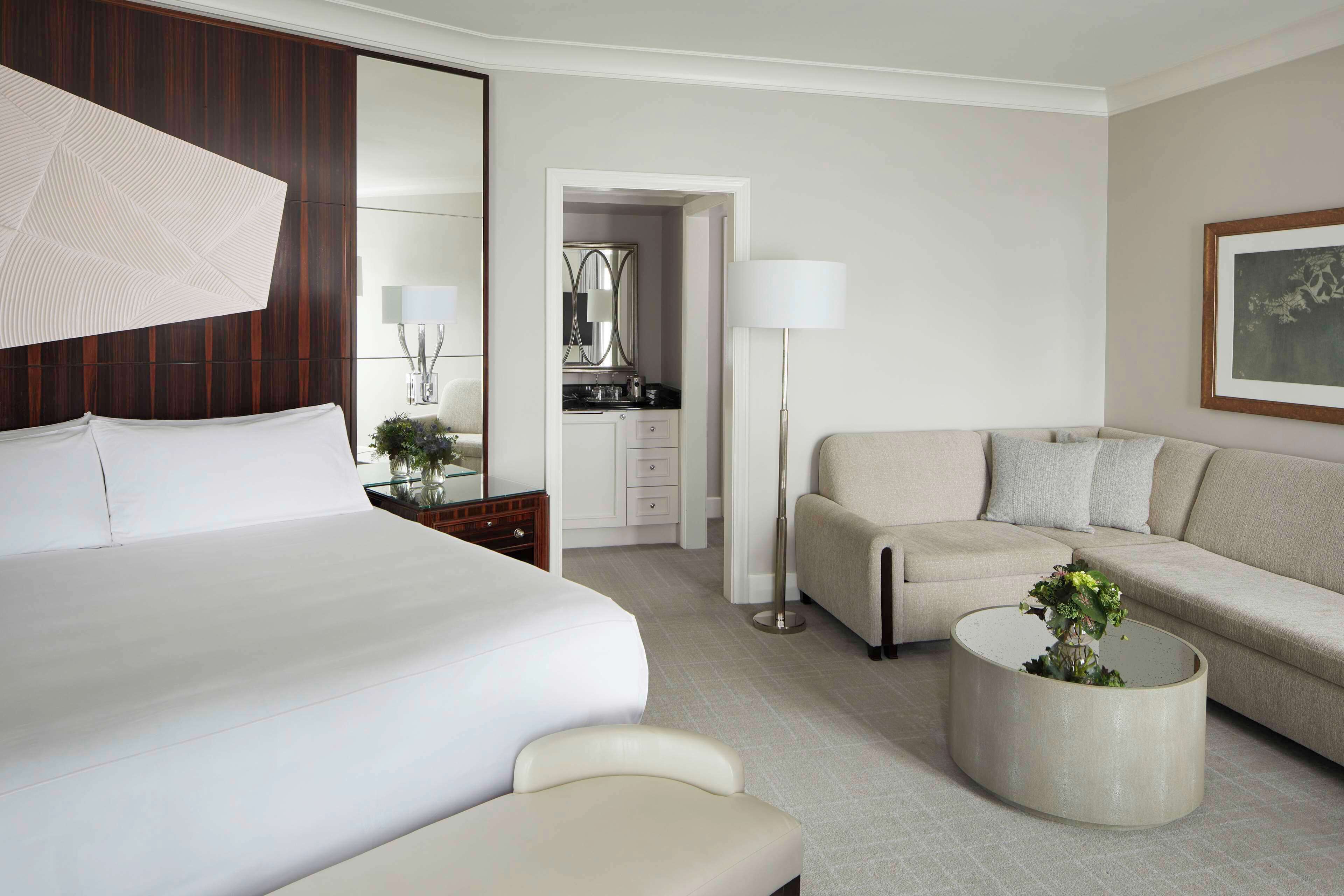 Une chambre d’hôtel avec un grand lit, un canapé, une table basse avec une plante, un miroir, une lampe et un tableau encadré au mur.