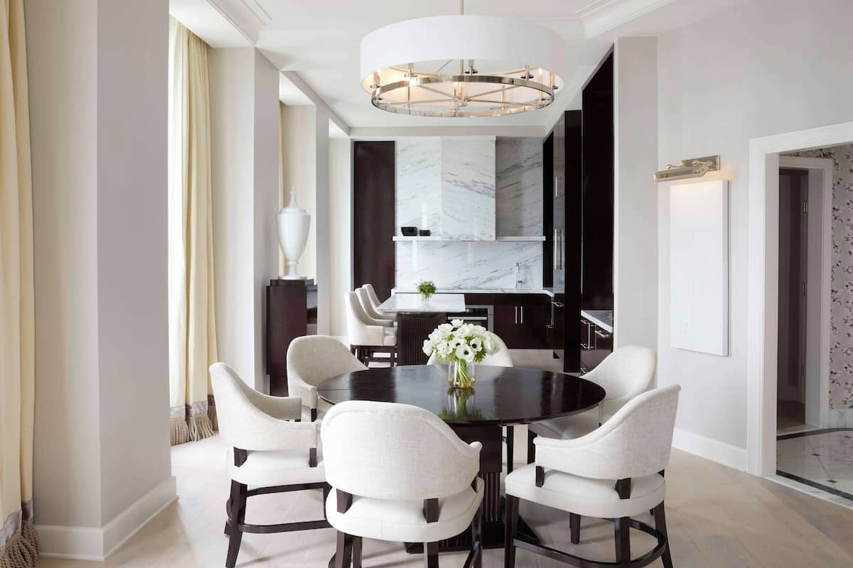 A modern dining area with a round table, white upholstered chairs, and a central chandelier.
