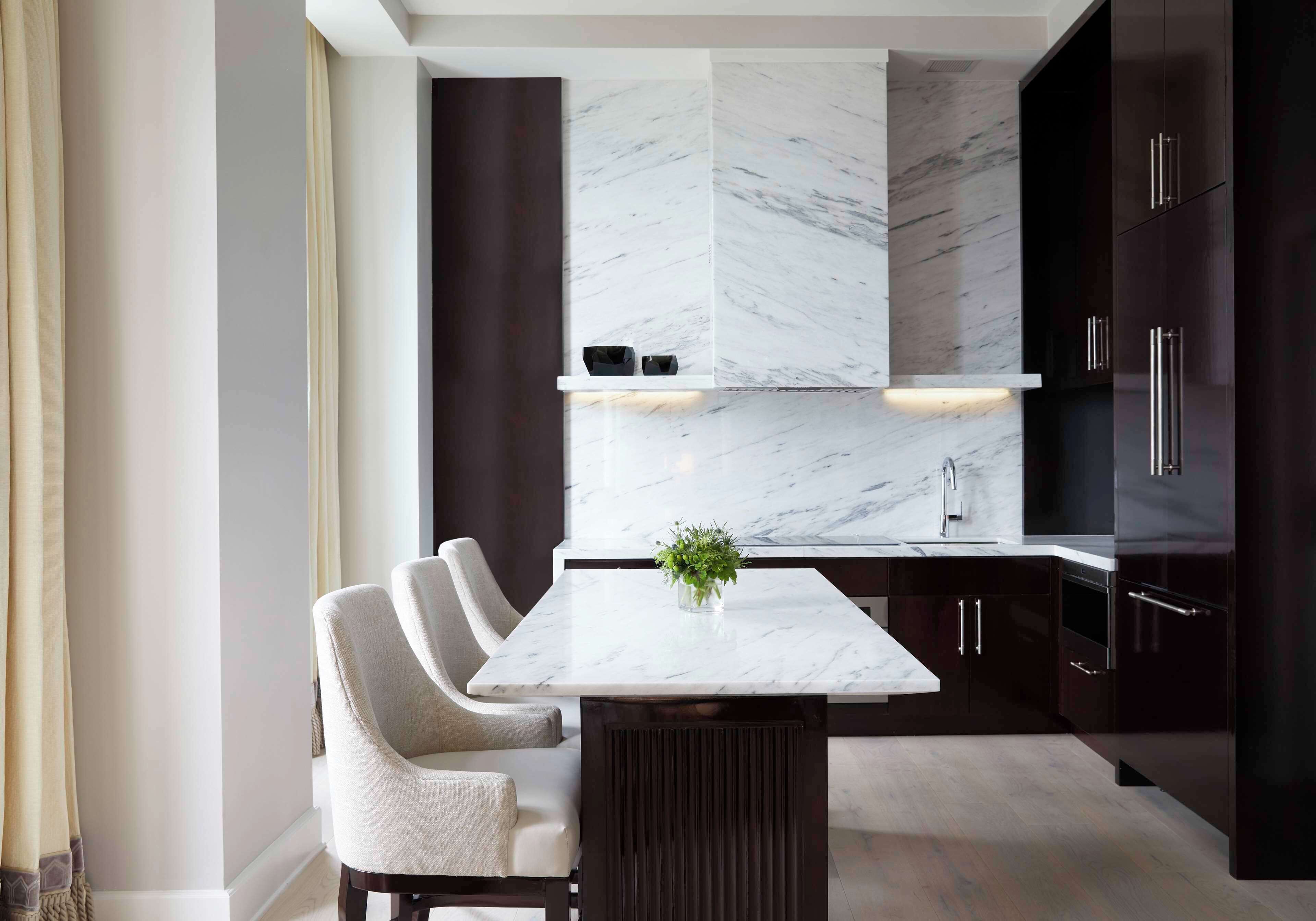 A modern kitchen with a marble countertop, dark cabinetry, and a central island with seating.