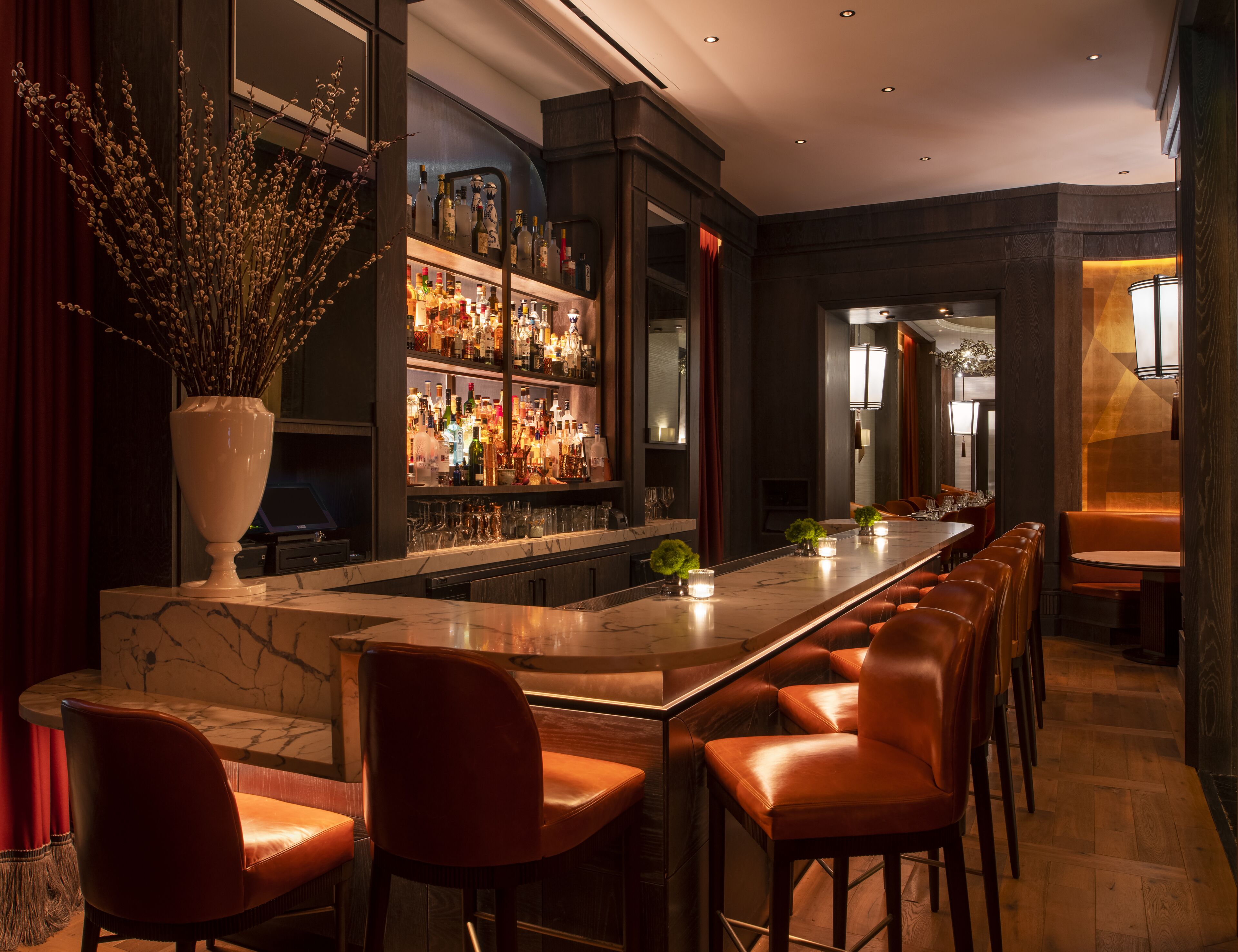 A bar area with a marble countertop, leather bar stools, and a variety of bottles.