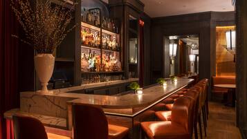 A bar area with a marble countertop, leather bar stools, and a variety of bottles.