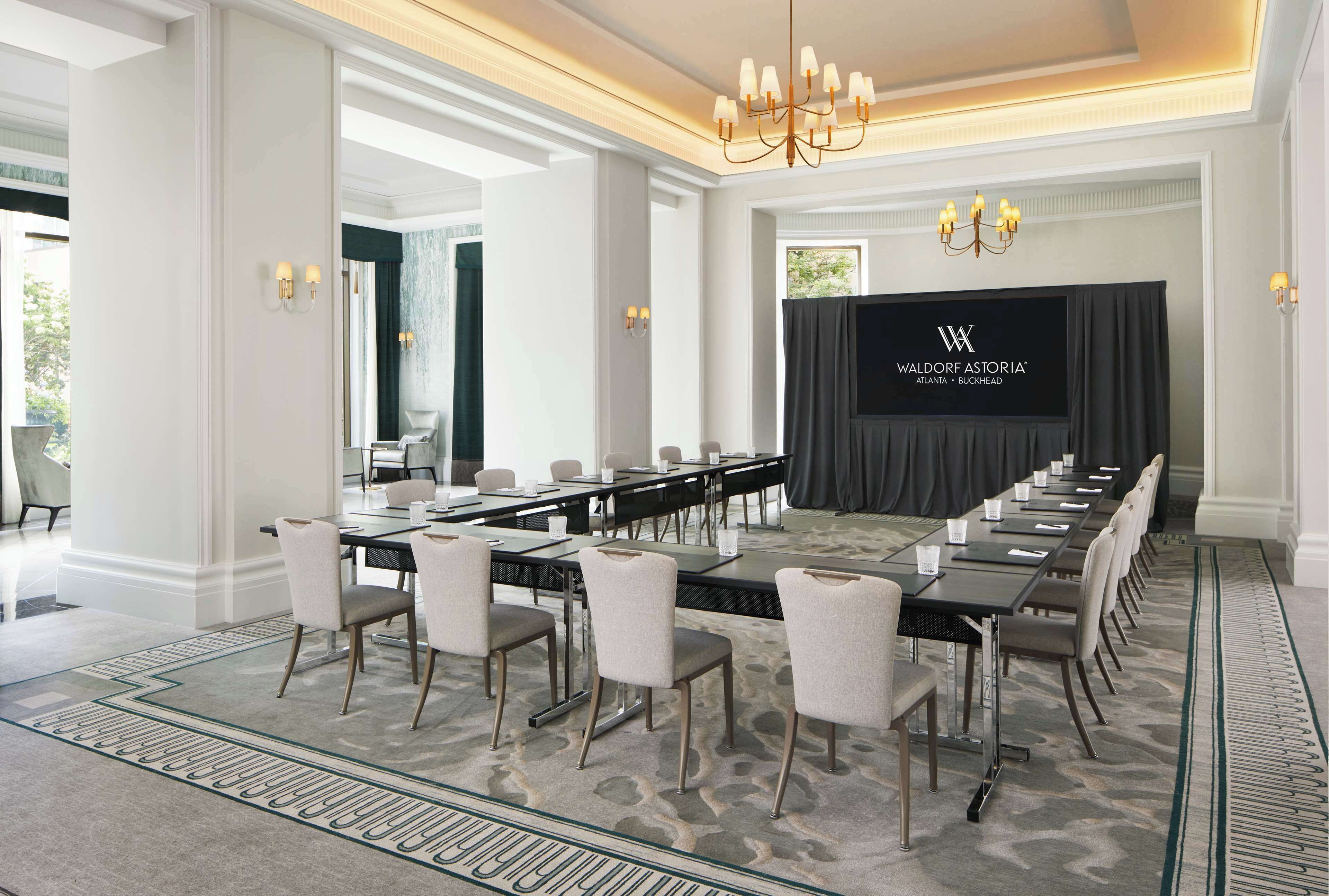 Een vergaderzaal met een lange tafel, stoelen, een kroonluchter en een scherm waarop de naam van het hotel staat.