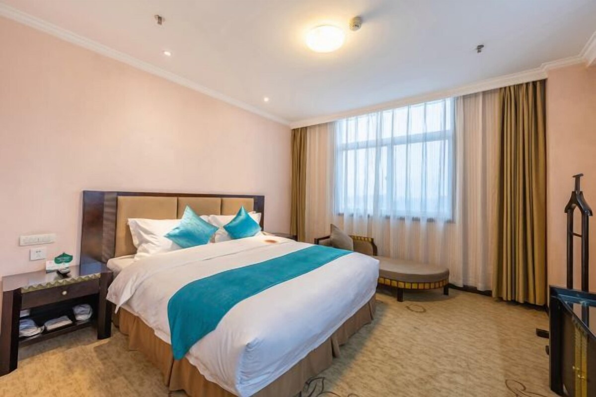 A hotel room with a large bed, a bedside table, a chair, a TV, and a window with curtains.