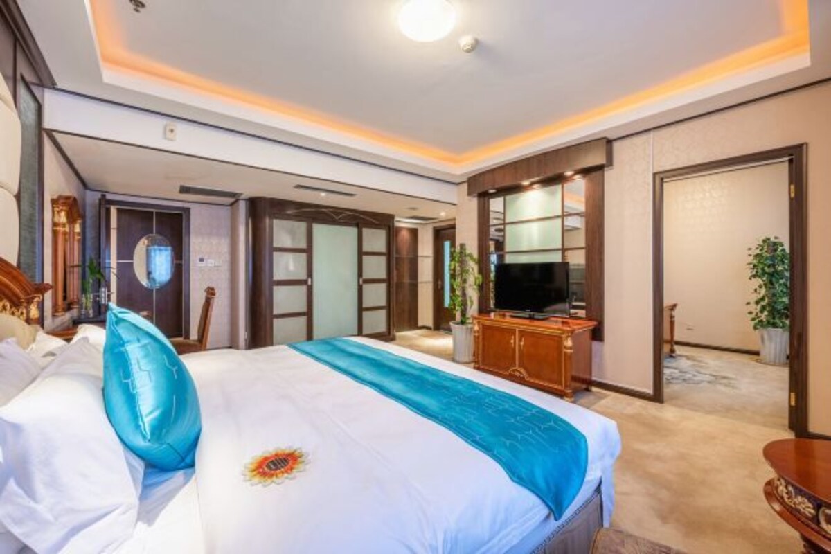 A hotel room with a large bed, a television, a wooden cabinet, and a plant.