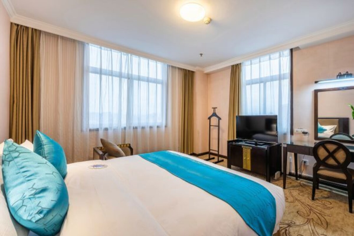 A hotel room with a large bed, a desk with a computer, a chair, a TV, and a mirror.