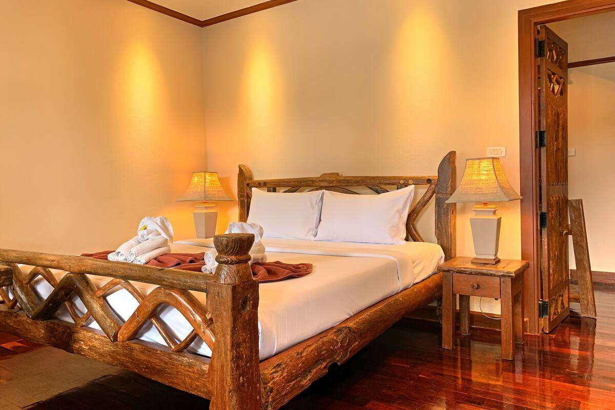 Una cama de madera con cabecera, dos mesitas de noche con lámparas y una silla de madera.