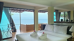 Habitación de hotel con una cama grande, vista al mar, terraza de madera y balcón con silla y mesa.