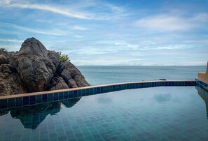 Relax by the infinity pool overlooking the ocean and a striking rock formation.