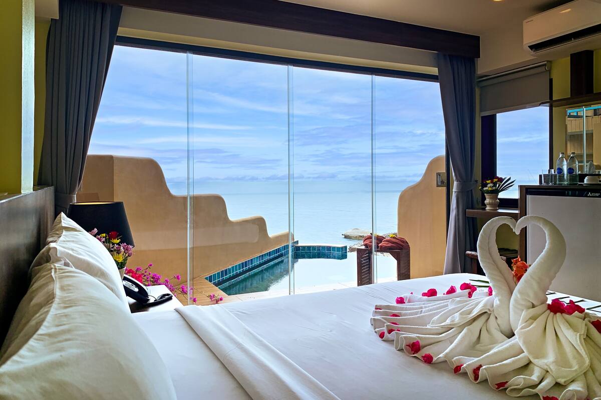 Habitación de hotel con una cama grande, vista al mar y un balcón con piscina.