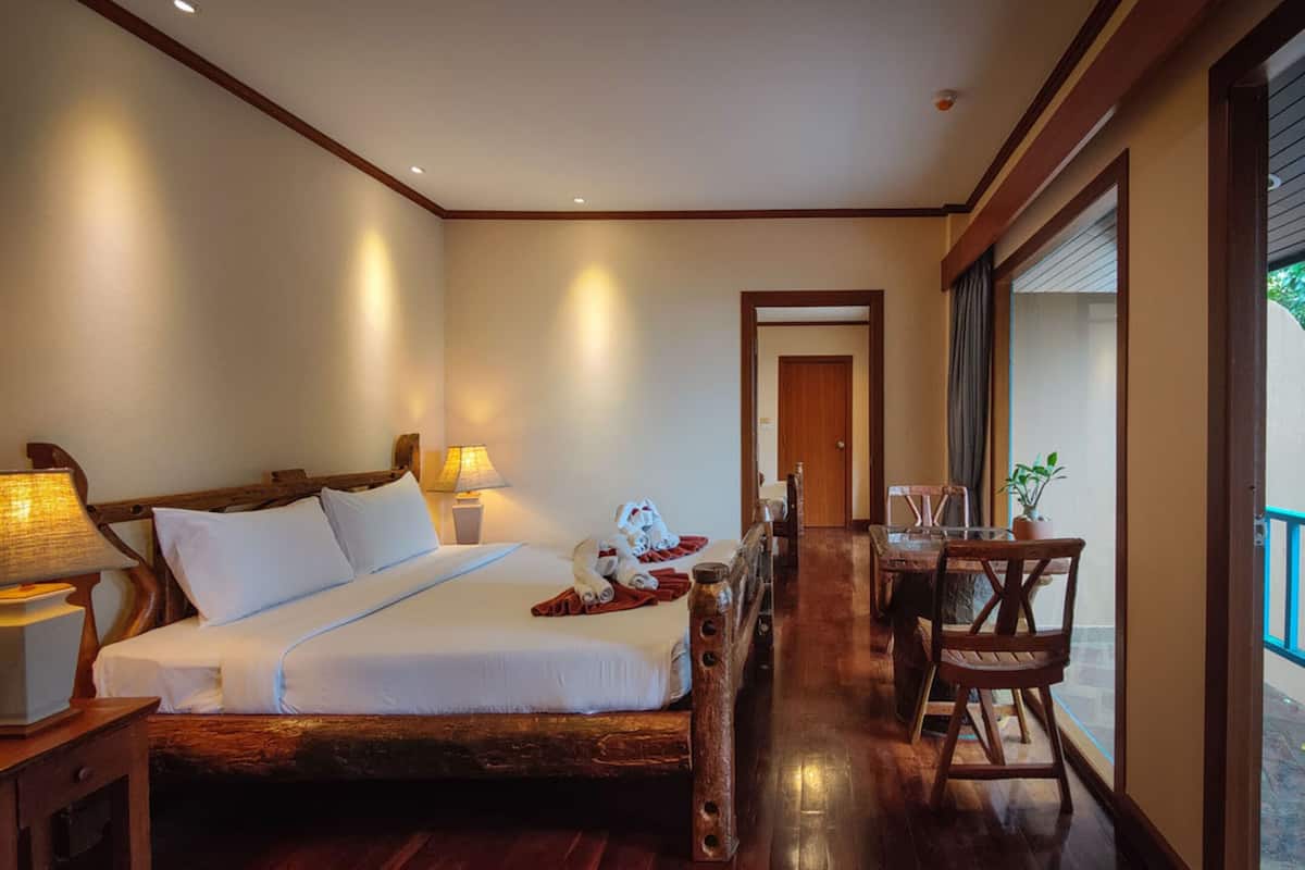 Una habitación con cama de madera, lámparas de noche, una mesa de comedor con sillas y vistas amplias por un gran ventanal.