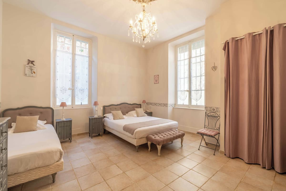 Une chambre à coucher avec un grand lit, deux tables de chevet, un banc, une chaise et un lustre.
