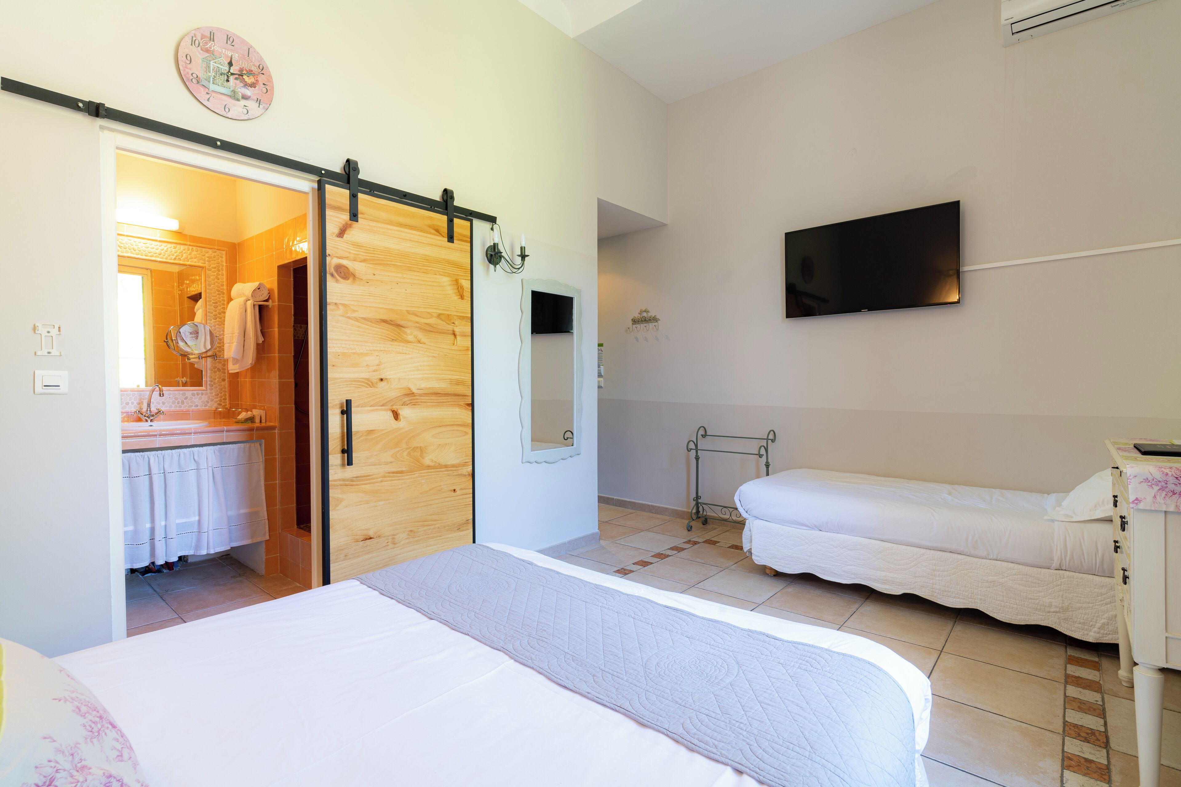 A bedroom with a large bed, a smaller bed, a wooden wardrobe, a television, and a bathroom visible through an open door.