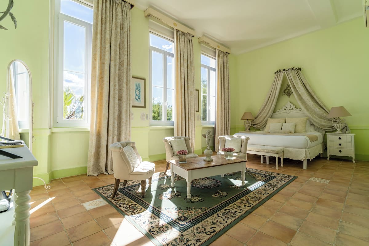 Une chambre à coucher avec un lit, une table de chevet, une chaise, une table et une fenêtre avec des rideaux.