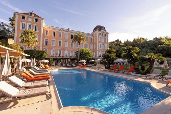 A swimming pool with lounge chairs and umbrellas, surrounded by a large building with multiple windows and a dome. - Hotel L Orangeraie (La Croix-Valmer)