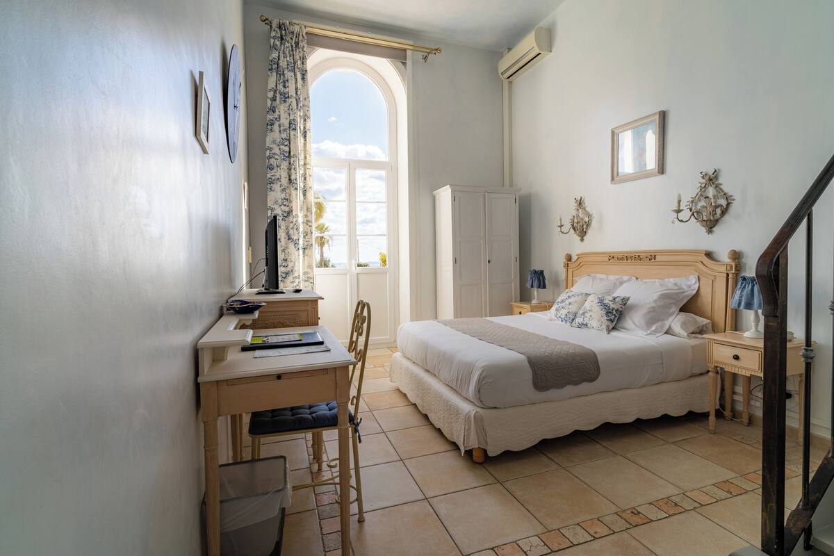 Une chambre à coucher comprenant un lit, un bureau, une chaise, une armoire et une fenêtre donnant sur un paysage agréable.