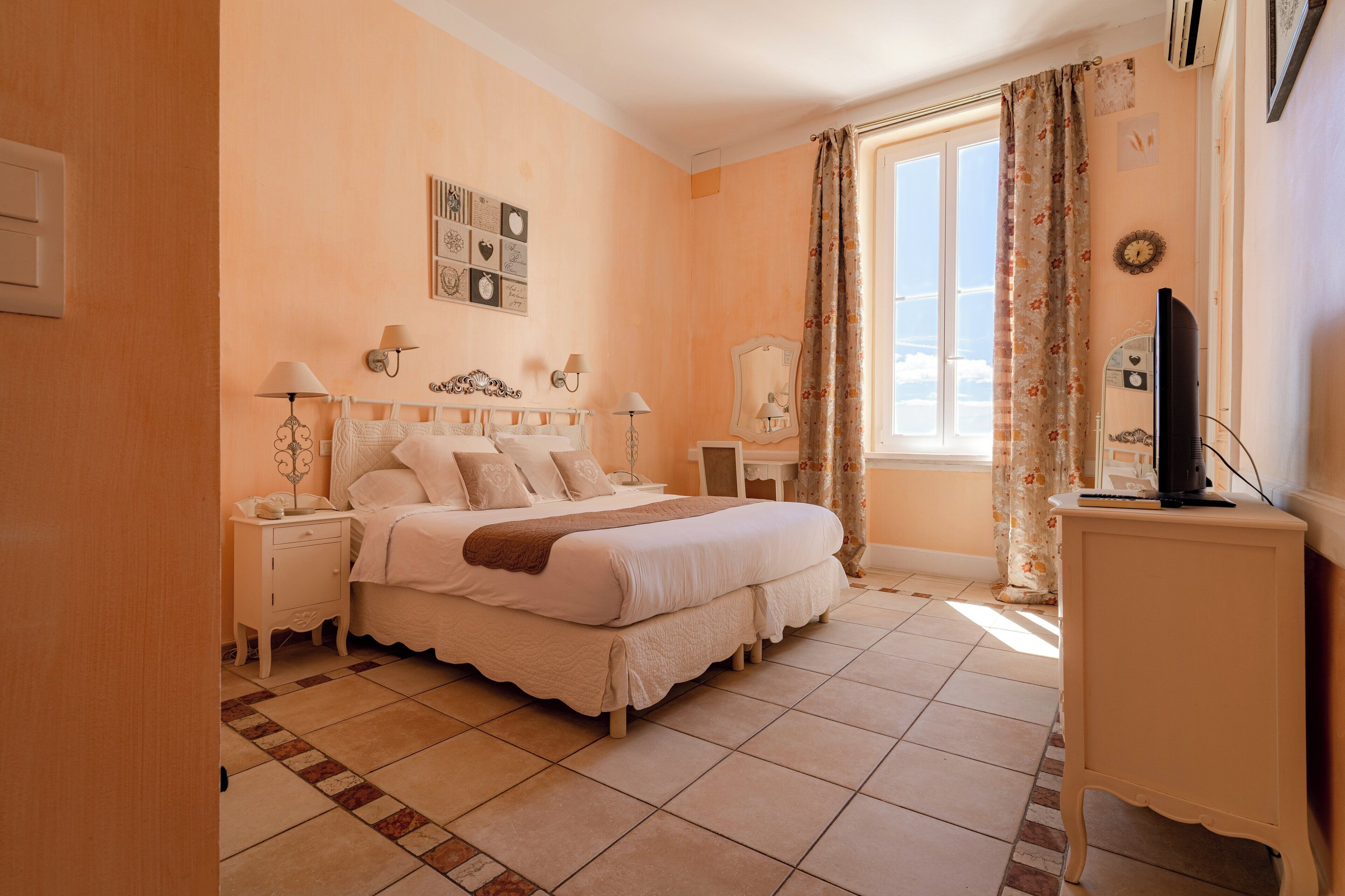 A bedroom with a large bed, bedside tables, a TV, and a window with curtains.