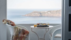 Un balcón con sillas de mimbre, una pequeña mesa con desayuno y vistas al mar y a los acantilados.