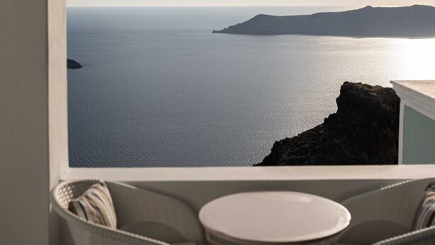 Vista desde un balcón con mesa y sillas, con vista al mar tranquilo y la costa lejana.