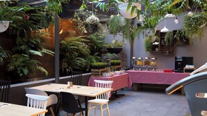 An outdoor dining area with tables and chairs, surrounded by lush greenery and hanging plants. - Metro Aspire Hotel, Sydney (Ultimo)